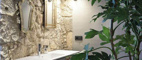 A bathroom with a stone wall, a white sink, and two mirrors.