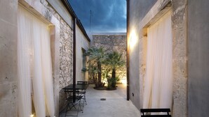 A narrow courtyard with stone walls, a palm tree, and a table with chairs. - Isonzo Suites (Syracuse)