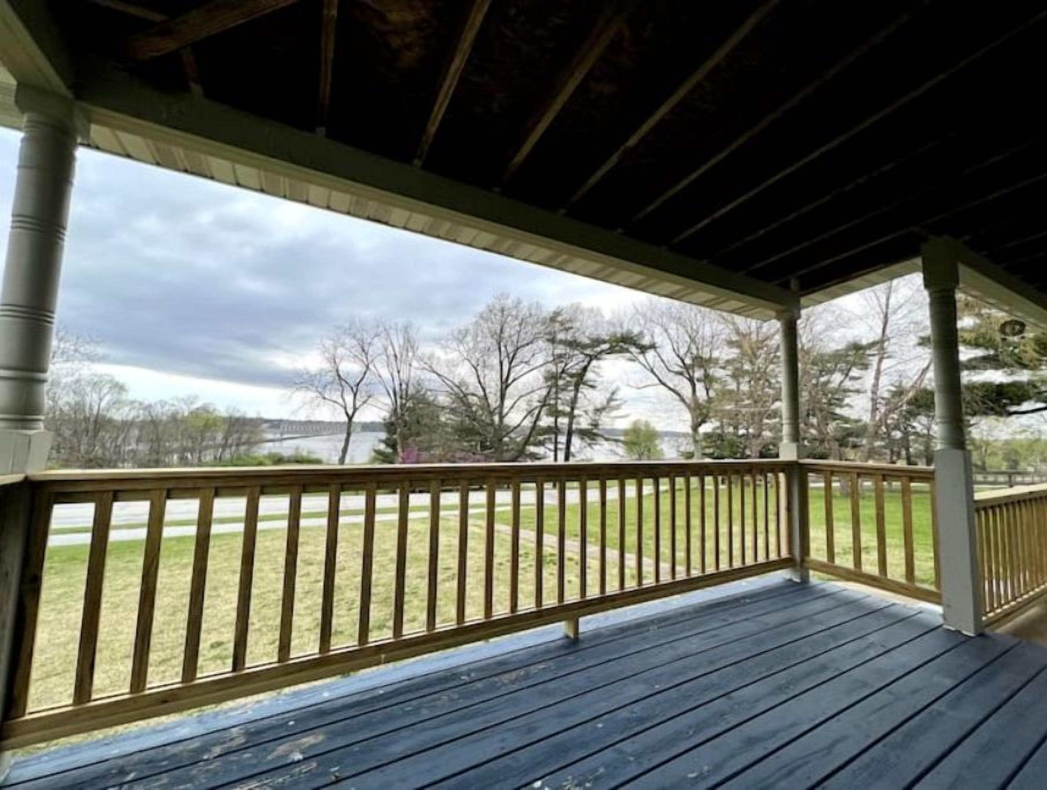 A covered porch with a view of a grassy yard and trees.