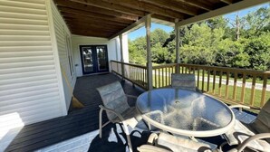 Une véranda avec une table et des chaises à plateau en verre, une terrasse en bois et une vue sur la verdure.