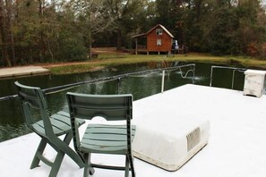 A dock with two green chairs and a white heater, overlooking a calm body of water with a wooden cabin in the background. - A Shore Bet 36' Vintage Houseboat. (Bogalusa)
