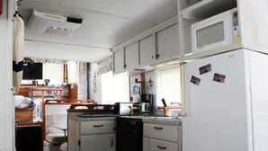 A compact kitchen with a microwave, stove, and refrigerator. There is a small dining area with a table and chairs. - A Shore Bet 36' Vintage Houseboat. (Bogalusa)