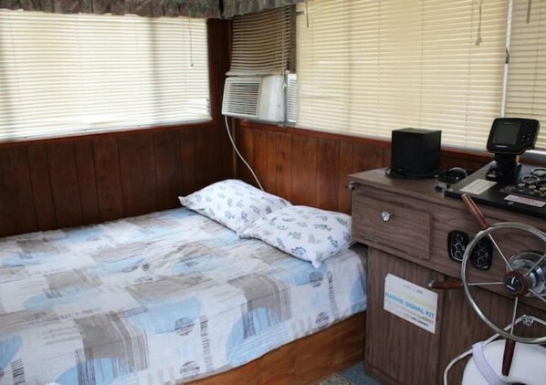 A small cabin with a single bed, a wooden desk with a marine signal kit, and an air conditioning unit. - A Shore Bet 36' Vintage Houseboat. (Bogalusa)
