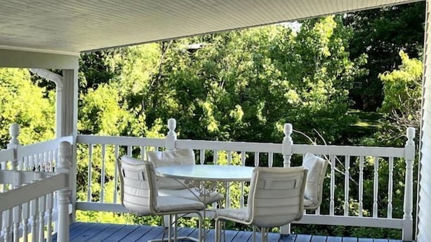 A covered outdoor seating area with a table and four chairs, surrounded by a white railing and a view of green trees. - Riverview Orchard 2: Master Suite Studio Style (Hamilton)