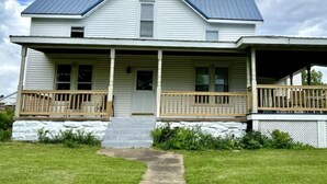 A two-story house with a front porch, a covered front porch area, and a stone foundation. - Riverview Orchard 2: Master Suite Studio Style (Hamilton)