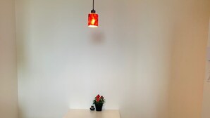 Un pequeño comedor blanco con una mesa, dos taburetes, una lámpara colgante roja y una planta en maceta sobre la mesa.