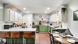 A modern kitchen with green cabinets, a central island with stools, stainless steel appliances, and a dining area with a wooden table and chairs. - Dog Friendly, 3 Bedrooms, Hot Tub, Peaceful & Private, Mini Golf, Coffee Bar! (Sevierville)