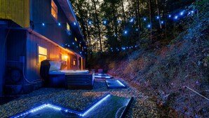 A wooden cabin with a hot tub and string lights in a forested area. - Dog Friendly, 3 Bedrooms, Hot Tub, Peaceful & Private, Mini Golf, Coffee Bar! (Sevierville)