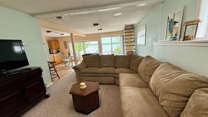 Un salon comprenant un canapé d’angle, un meuble de rangement en bois foncé pour l’équipement audiovisuel et une petite table d’appoint en bois.