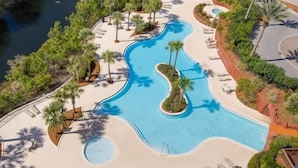 An aerial view of a resort with a large, winding pool surrounded by palm trees and lounge chairs.
