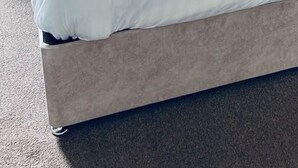 Una cama bien tendida con sábanas blancas, cabecera gris y dos almohadas decorativas.