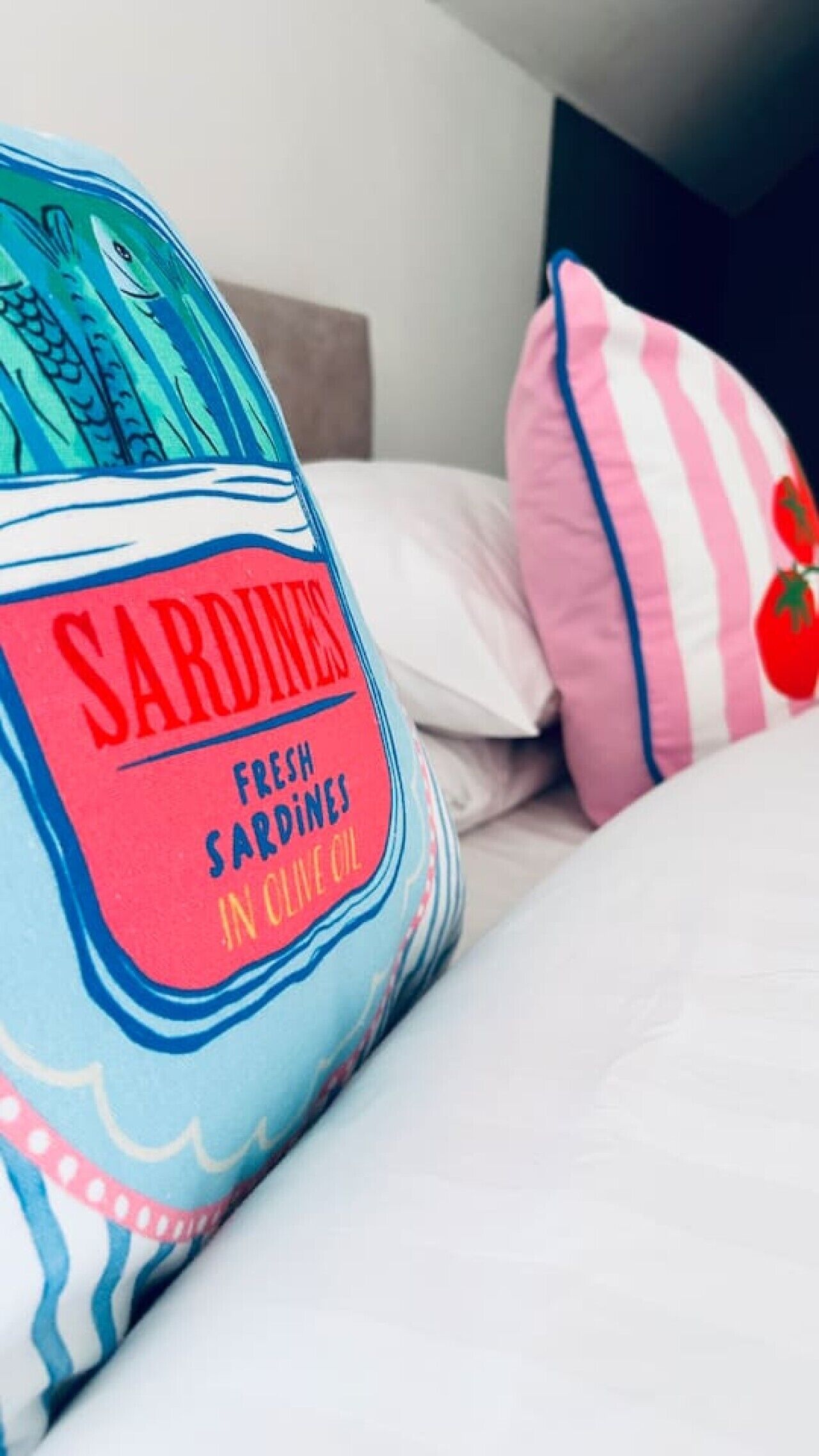 A bed with a blue and pink striped pillow and a pillow with a tomato design.