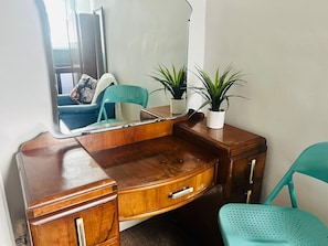 A wooden vanity with a mirror, a teal chair, and two potted plants.