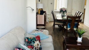 Una sala de estar con sofá, mesa de comedor, sillas, lámpara y planta.