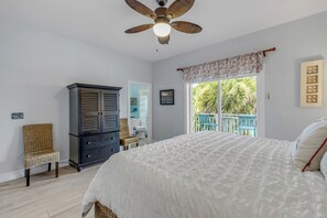 Un dormitorio con cama, armario, silla, ventilador de techo y ventana con vistas a follaje.