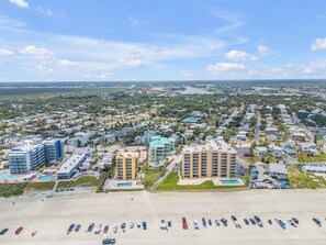 A coastal cityscape with a beachfront hotel featuring multiple floors, a swimming pool, and a parking lot.