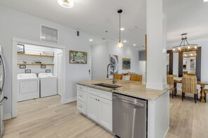 A modern kitchen with built-in appliances, a central island, and a dining area with wicker chairs. - •Oceanfront Condo •3BR 3BA •Heated Pool • Easy Walk to Flagler Ave (New Smyrna Beach)