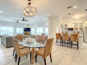 A spacious kitchen with white cabinets, a central island, and a dining area with wicker chairs and a glass table. - •Oceanfront Condo •3BR 3BA •Heated Pool • Easy Walk to Flagler Ave (New Smyrna Beach)