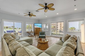 A spacious living room with a large sofa set, a television, and a ceiling fan.