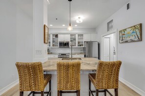 A modern kitchen with white cabinets, a central island with bar stools, and a painting of a beach scene.