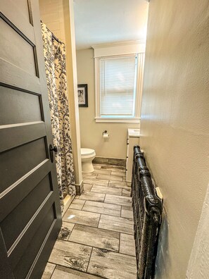 A narrow hallway with a wooden floor leading to a bathroom with a toilet and a window with blinds. - "The Red House" 4 Bedroom/Sleeps 8 in the heart of Albany NY (Albany)