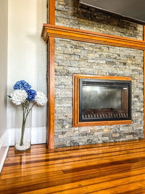 A stone fireplace with a wooden frame, a clear glass door, and a vase with blue and white flowers on the floor. - "The Red House" 4 Bedroom/Sleeps 8 in the heart of Albany NY (Albany)