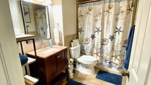 A bathroom with a toilet, sink, mirror, and shower curtain with a sea-themed design. - Main St. Retreat (Safety Harbor)
