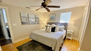 A bedroom with a bed, a ceiling fan, a window, and artwork on the wall. - Main St. Retreat (Safety Harbor)
