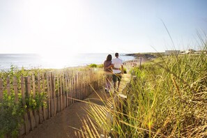A pathway leading to a beach with a wooden fence and tall grass.