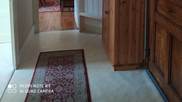 Ein Flur mit einem Holzschrank, einer weißen Wand mit Haken und einem roten und weißen Teppich.