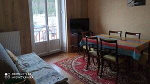 Ein Zimmer mit einem Bett, einem Esstisch mit Stühlen, einem Fernseher und einem Fenster mit Blick auf Gebäude und Bäume.