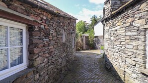 Een smalle, geplaveide steeg tussen stenen gebouwen, met een raam aan de linkerkant.