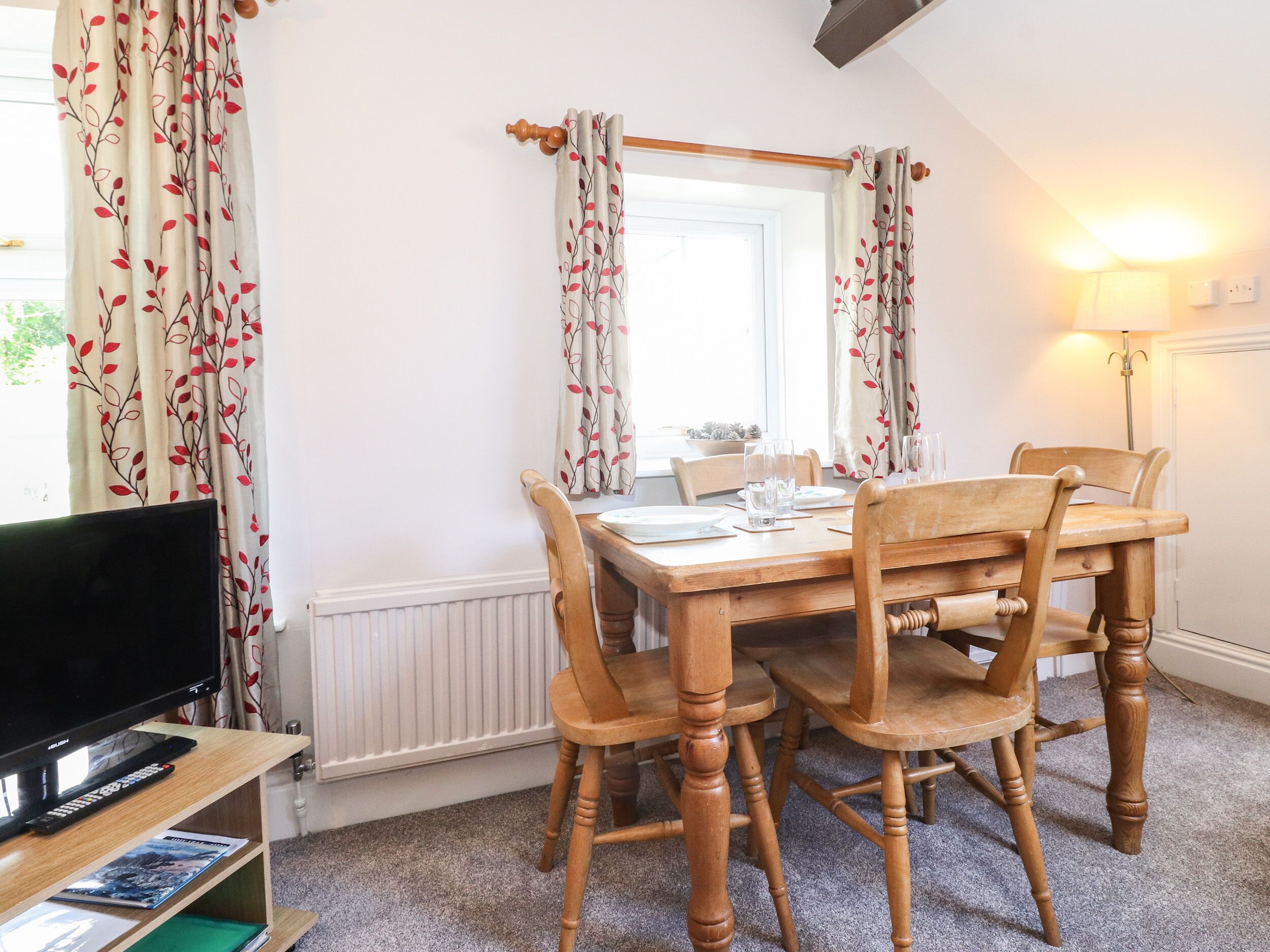 A dining area with a wooden table set for four, a television on a stand, and a radiator below.