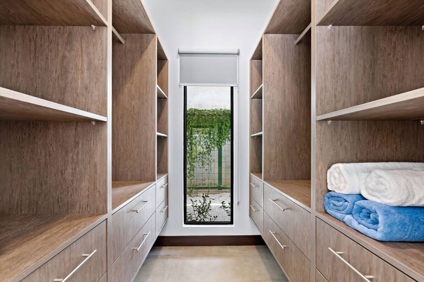 Ein begehbarer Kleiderschrank mit Holzböden und Schubladen, Blick auf Grün im Freien und ordentlich gefaltete Handtücher auf der rechten Seite.