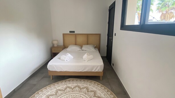 A bedroom with a bed, a bedside table, a window, and a patterned rug. - Le Pied à Terre N°3 (Grosseto-Prugna)