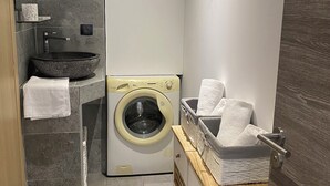 A compact bathroom with a washing machine, a sink with a stone basin, and a towel rack. - Le Pied à Terre N°3 (Grosseto-Prugna)
