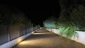 A nighttime pathway flanked by greenery and illuminated by overhead lights. - Le Pied à Terre N°3 (Grosseto-Prugna)