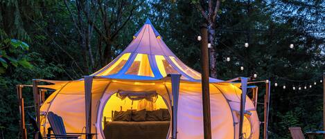 Een tent met een kegelvormig dak, een bank en een tafel met stoelen ervoor.