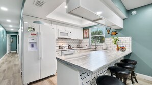 Una cucina moderna con mobili bianchi, un'isola centrale con sgabelli da bar, un forno a microonde e un lavandino.