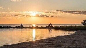 Un tramonto su un'acqua calma con un litorale roccioso e alcune persone in riva al mare.