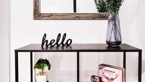 Ein schwarzer Metallkonsole mit einem Spiegel darüber, einer Vase mit Grünpflanzen und einem Schild mit der Aufschrift 'hello'.