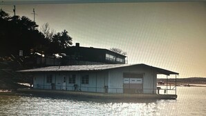 A waterfront house with a garage, a balcony, and a dock extending into the water. - Retro Lakefront Cabin with Lots of Amenities (Tow)