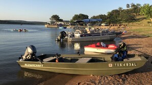 A boat named ALUMACRAFT docked at a lakeside with other boats and a covered area in the background. - Retro Lakefront Cabin with Lots of Amenities (Tow)