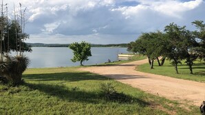 A lakeside path with a dirt road leading to a grassy area, surrounded by trees and a clear sky. - Retro Lakefront Cabin with Lots of Amenities (Tow)
