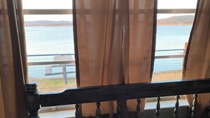 A bed with a wooden headboard, a view of a lake through sheer curtains, and a wooden railing outside. - Retro Lakefront Cabin with Lots of Amenities (Tow)