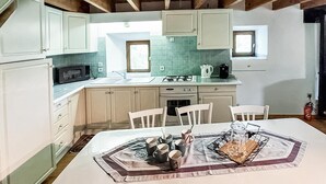 Una cocina con armarios blancos, una estufa y un fregadero. Hay una mesa con un mantel individual y tazas.