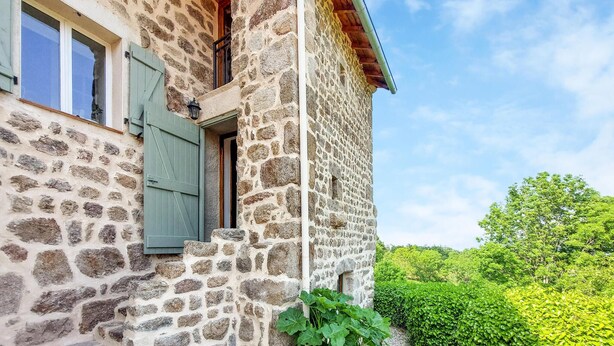Un edificio de piedra con un balcón, una ventana con contraventanas y vistas al verdor.