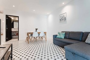 A modern living room with a black and white patterned floor, a grey sofa with patterned cushions, a dining table with chairs, and a wall-mounted artwork. - Casa Lefevre 3C (Panama City)