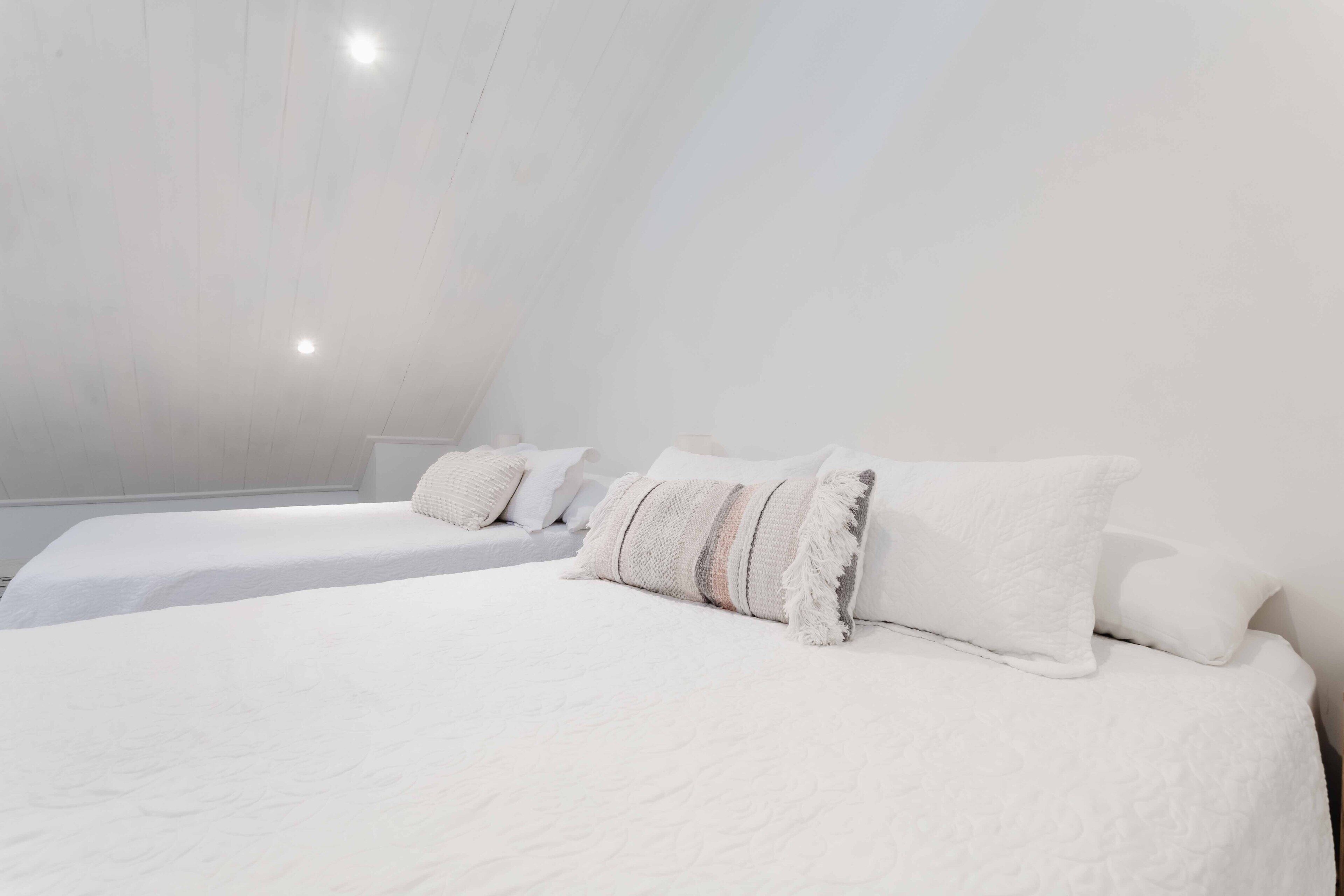 A bedroom with two beds, white bedding, and a sloped ceiling.
