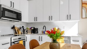 Una cocina moderna con gabinetes blancos, una estufa de acero inoxidable y un microondas. Hay una mesa de comedor de madera con un jarrón de tulipanes.